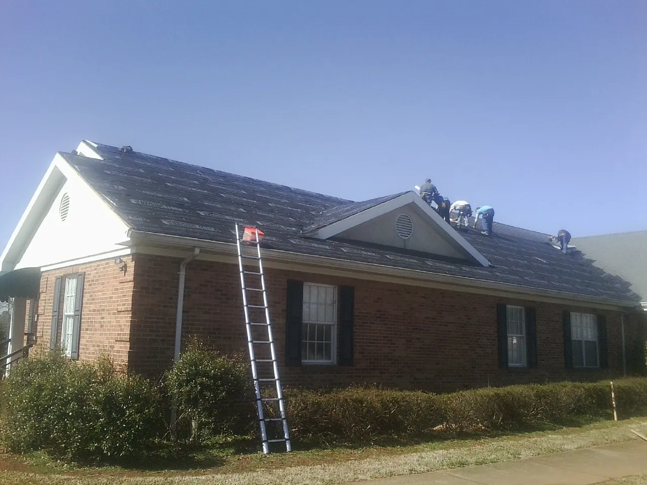 Crew tearing shingles off a brick ranch roof with a ladder set — Metal Roof Repair work by our crew in Forestburgh