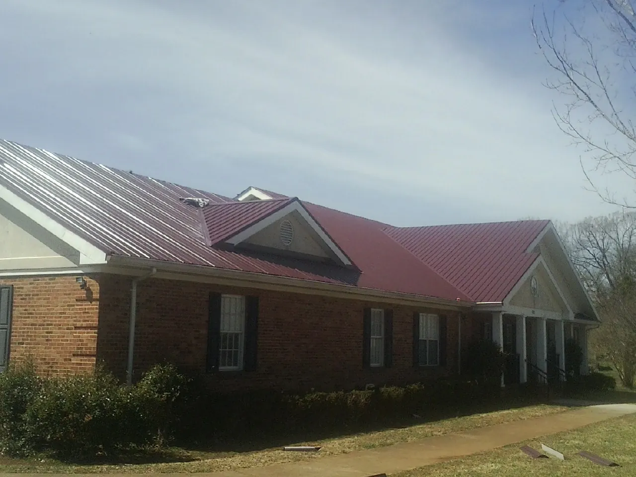 Red metal roof with gabled entries on a long brick building, from a Hail Damage Roof Repair job in Forestburgh