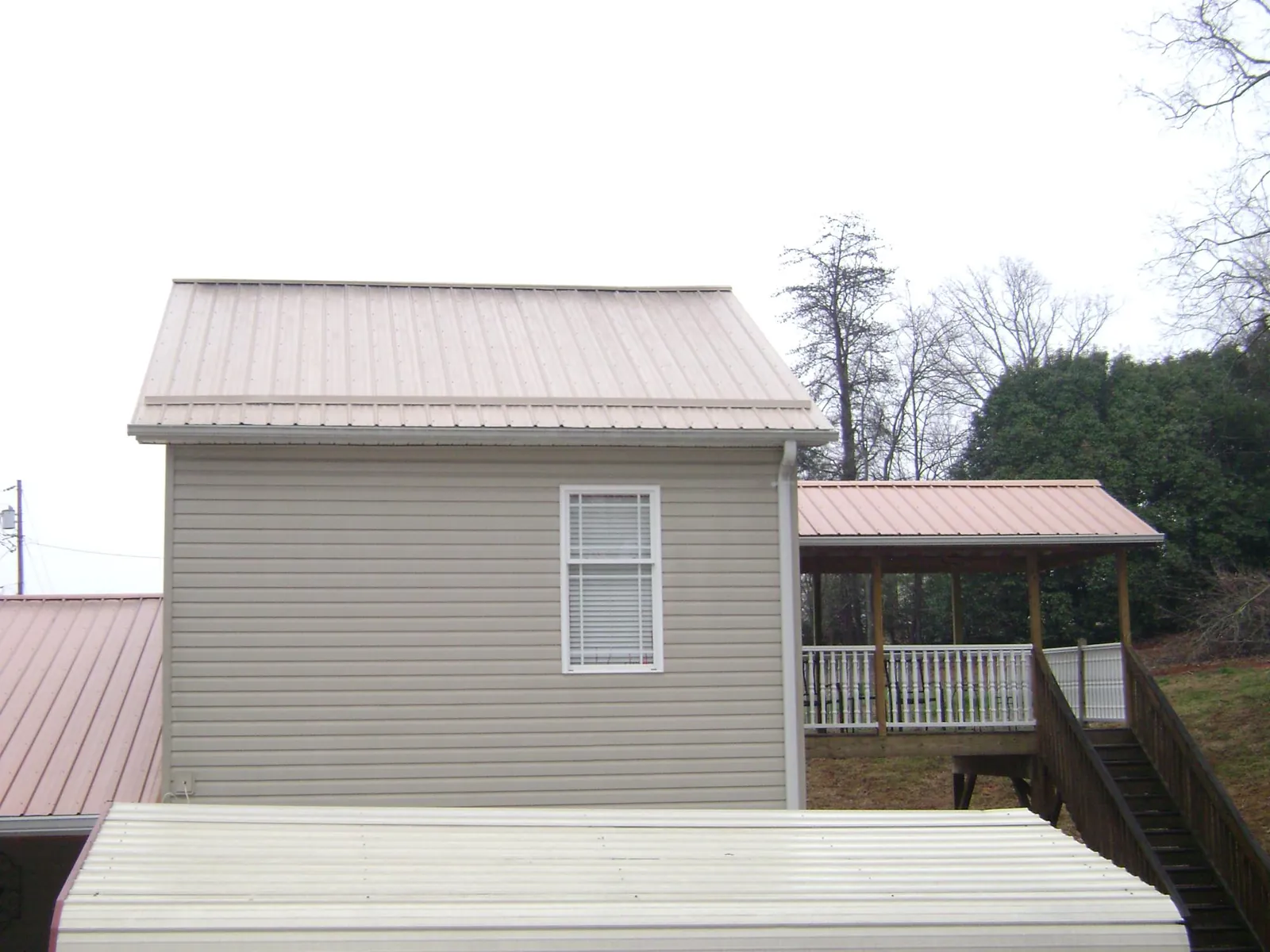 Tan metal roofs on a two story addition and attached porch, from a Roof Replacement job in Forestburgh